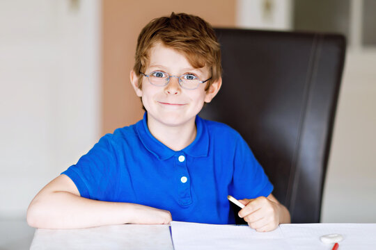 Cute little kid boy with glasses at home making homework, writing letters with colorful pens. Little child doing exercise, indoors. Elementary school and education, imagine fantasy concept