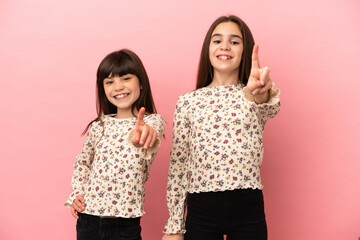 Little sisters girls isolated on pink background showing and lifting a finger