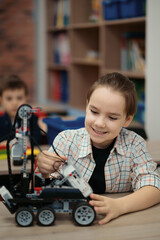 Two kids of different age choose parts of robotic electric toys for building robots at robotics school lesson.