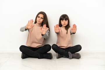 Little sisters sitting on the floor isolated on white background making stop gesture for disappointed with an opinion