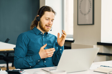 Young man professional call center operator wearing headset looking at laptop screen and talking...