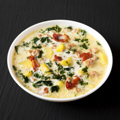 Homemade Zuppa Toscana with Kale and Bread in a white bowl on a black background, side view.