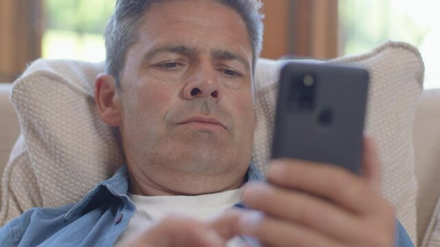 Close Up Shot of a Middle Aged Man Slouched On a Sofa Using Smartphone 
