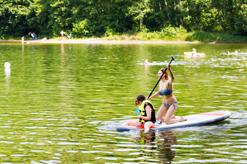 Young woman with school girl paddling on sup board on a lake. Active family on modern trendy stand...