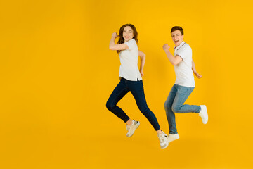 Fototapeta na wymiar Portrait of a young happy couple man and woman in white t-shirts jumping and laughing on a yellow background.