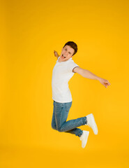 Portrait of a young happy man in white t-shirt smiling and jumping on a yellow background.