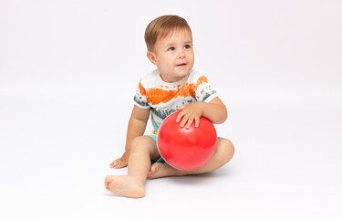 Fototapeta na wymiar Playful cute little baby boy dressed in a striped bodysuit, sitting and playing a new ball on a white background. Concept of children's games. Place for text. Active childhood concept.