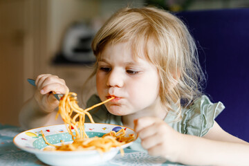 Adorable toddler girl eat pasta spaghetti with tomato bolognese with minced meat. Happy preschool...