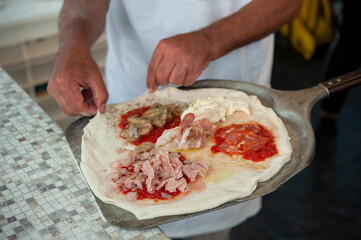 Pizzaiolo puts a four season pizza on the peel, ready to bake. Italian pizzeria.