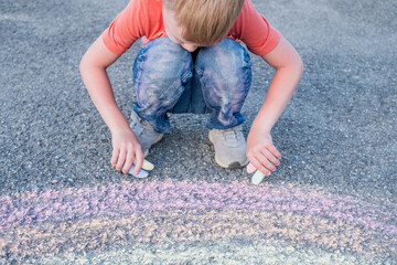 Fototapeta premium Boy with both hands draws a rainbow on the sidewalk on the pavement