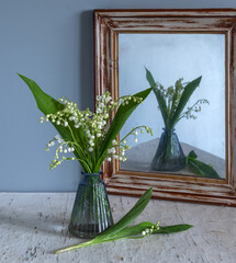 A small spring bouquet is reflected in an old and crooked mirror in a wooden frame.