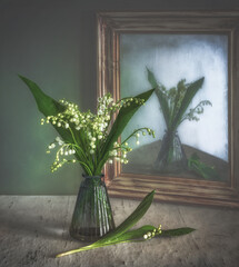 A small spring bouquet is reflected in an old and crooked mirror in a wooden frame.