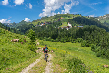 Fototapeta na wymiar happy senior woman riding her electric mountain bike up to thr famous mountain village of Damuels in the Bregenz Forest mountain of Vorarlberg, Austria
