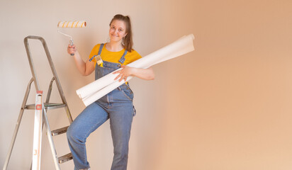 Happy young woman holding wallpaper rolls on ladder with roller. DIY home apartment renovations.