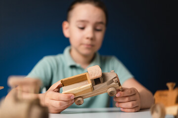School boy playing, hands holding with wooden toys on white table, while staying at home on blue enlighted background