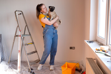 Happy woman makes repairs in her apartment with her funny pug dog. happiness in anticipation of a...