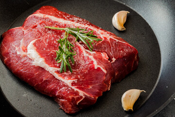 Raw beef steak with rosemary and garlic in a pan