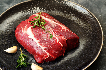 Raw beef steak with rosemary and garlic in a dark plate.