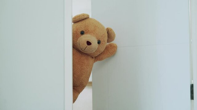Concept for kid. A brown teddy bear poked his face from behind the wall. The brown teddy bear poke a face next to the door the face of teddy bear look smile. teddy bear hidden inside the room.