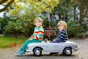Two little preschool boys playing with big old toy car in summer garden, outdoors. Happy children play together, driving car. Outdoor activity for kids. Siblings and friends on warm day