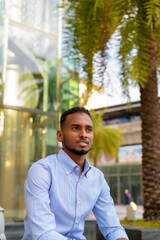 Portrait of handsome black African businessman outdoors in city during summer sitting and thinking