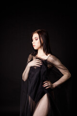 Fototapeta premium dark blond girl in a black dress wrapped in black chiffon stands half a turn