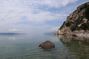 Seascape calm at sea in a picturesque bay on the sea coast of Croatia on a summer day. Calm clear water of the Adriatic Sea, in which clouds are reflected and stones are visible at the bottom 