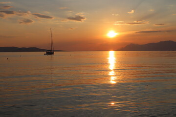 Fototapeta na wymiar Yacht on the sea on a summer evening against the backdrop of the setting sun, a mountain range on the horizon, Croatia