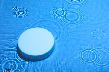 Empty white circle podium on transparent clear dark blue water texture with splashes and waves in sunlight. Abstract nature background for product presentation. Flat lay cosmetic mockup, copy space.