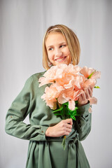 Young teen blonde girl with flowers and white studio background. Spring portrait. Healthy skin and natural makeup for teenage girls