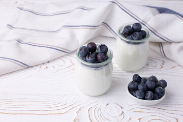 Greek yogurt in a glass jar and fresh blueberries on a rustic white table. Healthy food concept. Selective focus