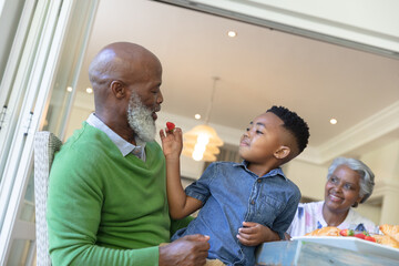 Happy african american grandson and grandparents sitting at table talking during breakfast