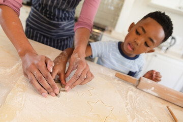 Obraz na płótnie Canvas Happy african american mother with son baking in kitchen, cutting cookies