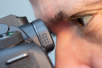 The photographer looks into the viewfinder of the camera, close up.