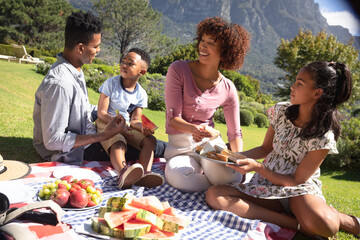 Happy african american couple with son and daughter outdoors, having picnic in sunny garden - Powered by Adobe