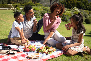 Happy african american couple with son and daughter outdoors, having picnic in sunny garden