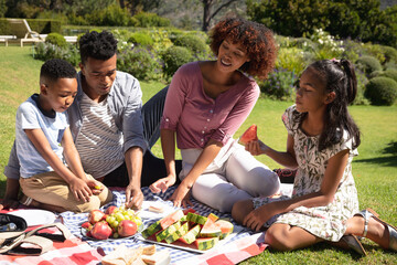 Happy african american couple with son and daughter outdoors, having picnic in sunny garden