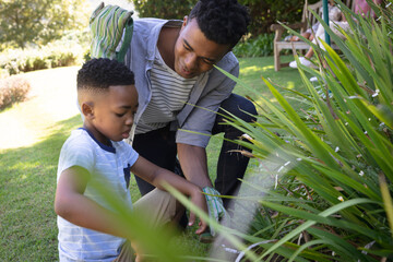Happy african american father with son outdoors, gardening on sunny day