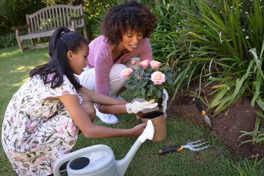 Happy african american mother with daughter outdoors, gardening on sunny day - Powered by Adobe