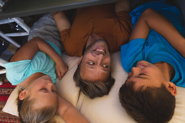 Caucasian father with daughter and son smiling, lying in blanket fort at home