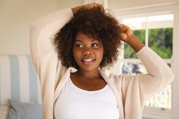 Portrait of smiling african american woman touching her hair sitting on sofa at home