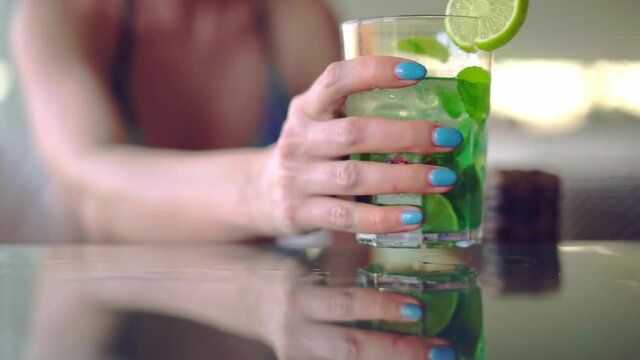 Woman in swimsuit sitting in poolside bar drinking mojito cocktail. Close view.