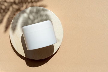 Mock-up of white jar for packaging cosmetics on round wooden stand with shadow from a palm branch....
