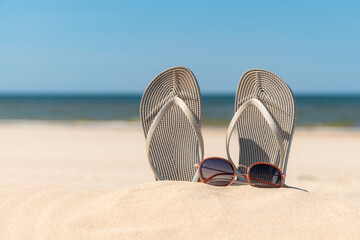 Grey sandals at the beach on a beautiful sunny day. Slippers in the sand by the sea. Flip flops at...