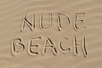 Nude beach letters written on the sand at the beach on a sunny day. Naked sunbathing. Naturalist lifestyle.