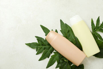 Fototapeta na wymiar Blank bottles of shampoo and leaves on white textured background