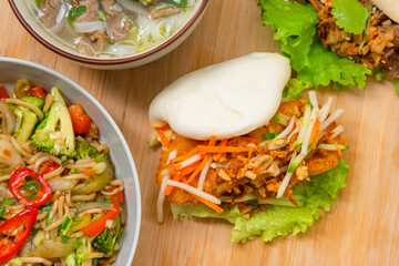 Delicious steamed bao bun on wooden table with fried chicken and fresh vegetables - salad, carrots and roasted peanuts. Popular street food