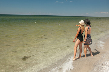 Fototapeta premium two women in swimsuits looking for a seashell on the seashore in the summer