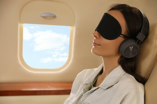 Young woman with sleep mask resting while listening to music in airplane during flight