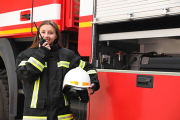 Firefighter in uniform using portable radio set near fire truck
